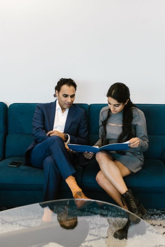 Two professionals discussing documents on a blue sofa in a modern office setting.