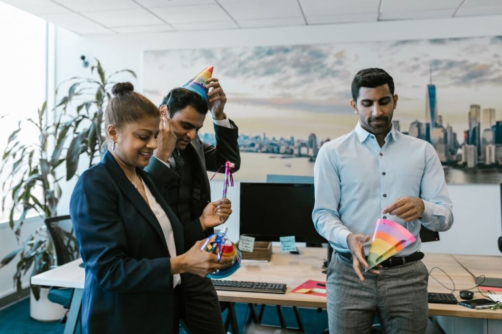 Three colleagues celebrating a birthday in the office with party hats and smiles.